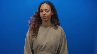 Genç bir kadın mavi stüdyoyu işaret ediyor. Tarafsız, kıvırcık saçlı, omuzları boyunca dalgalanan bir kazak giyiyor..