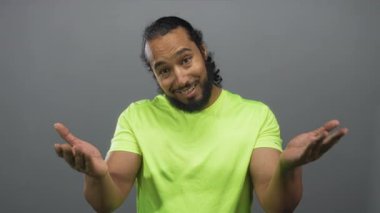 Stüdyoda gri arka plan ve neon yeşil tişörtle görülebilen el hareketlerini ve avuçlarını gösteren bir adam..