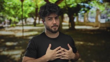 Yeşil parkta duran sakallı genç adam yazın dışarıda güneş ışığı altında duygularını ifade ediyor..