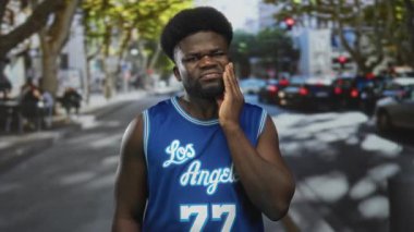 Şehir caddesinde, diş ağrısı için basketbol forması giyen bir adam, diş ağrısı çekiyor..