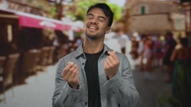 Canlı bir şehir caddesinde genç bir İspanyol adam para harcıyor, kendine güven ve enerji yayıyor, bulanık şehir arka planıyla açık hava ortamını güçlendiriyor..