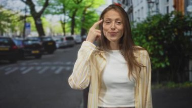 Genç İspanyol kadın, omuz silkme hareketiyle avuç içi kaldırırken ve hafifçe gülümserken parmak ucuyla caddeyi işaret ediyor..