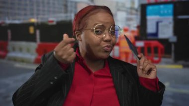 Kadın bize pasaport tutuyor ve şehir inşaatında gülümserken parmak kalp hareketi yapıyor; keyif yolculuğu.