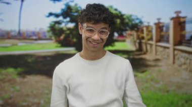 Parlak gün ışığı altında güneşli yeşil park çitlerine karşı el hareketleriyle hareket eden adam:.