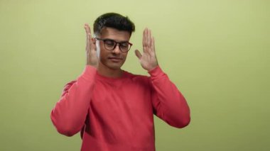 Kırmızı gömlekli genç adam, münferit bir portre oturumunda yaratıcılığını ve pozitifliğini ifade eden sarı arka planda ellerini kullanarak çerçeveleme hareketi yapıyor.