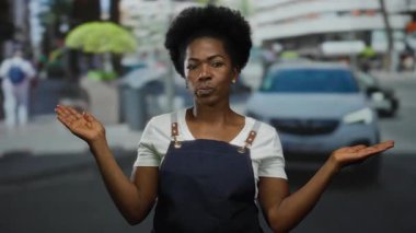 Önlük giymiş bir kadın hareketli bir şehir caddesinde kendinden emin duruyor, gücünü ve modern şehir yaşam tarzını aktarıyor..