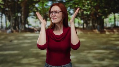 Parkta kızıl saçlı bir kadın, dışarıda gürültüden kulaklarını tıkayarak genç bir yetişkinin çevre sesine olan tepkisini çekici bir park ortamı ile doğal ortamda yakalıyor..