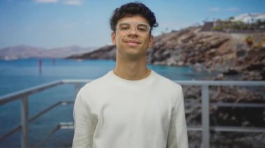 Beyaz kazaklı adam nazikçe gülümsüyor güneşli iskele korkuluklarında avuçlarını yukarı uzatıyor; dostça bir davet.