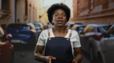 Yoğun şehir caddesinde, arka planda park halindeki arabalarla gün ışığında enerjik bir şekilde el kol hareketi yapan kadın..