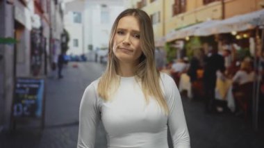 Şehir dışındaki terasta hareketli restoran arkaplanlarıyla zaman harcayan kadın, şehir mimarisi ve sosyal etkileşimin ortasında canlı bir sokak sahnesi sergiliyor..