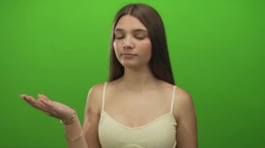 Genç kız stüdyo omuz silkme hareketinde yeşil zemine karşı el ele tutuşuyor; belirsizlik ikilemi ikilemi tereddüdü.
