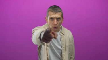 Kafkasyalı bir adam enerjik bir şekilde kameraya doğru hareket ediyor. Canlı pembe arka plan üzerinde bej gömleği var. Duygularını ve ifadelerini ifade ediyor..