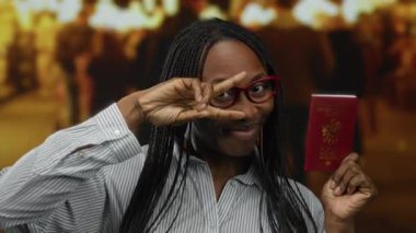 Gözlüklü bir kadın elinde parlak bir pasaport, hareketli bir şehir caddesinde sıcak bir gülümseme, bulanık ışıklarla çevrili, seyahat ve özgürlüğün özünü yakalıyor..