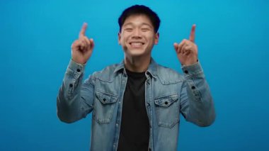 Genç adam gülümsüyor ve mavi bir arka plana doğru işaret ediyor.