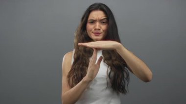 Gri stüdyo ortamında ara verme jesti ve ciddi ifade yapan kadın, duraksama duraksama endişesi.