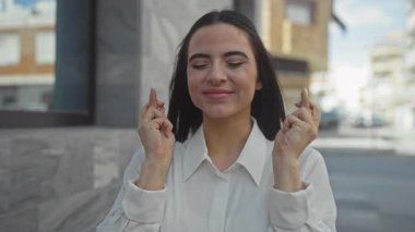 Umut dolu parmaklar üzerinde beyaz gömlekle gezen kadın şehir ortamında iyimserlik ve heyecan dolu bir ifade sergiliyor..