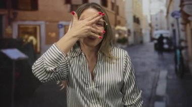 Avrupa 'nın dar kaldırım taşı caddesinde çizgili bluz ve gözlük takan kadın yüzünü gizler;.