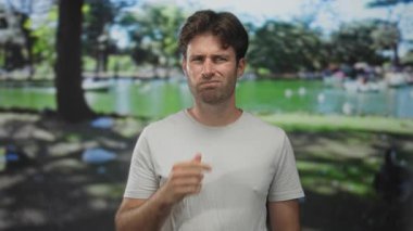 Parkta eli çenesinde bir adam yeşil bir gölet yanında, kulağı açık havada, dinleme için ayarlı; düşünceli yansıma.