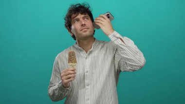 İspanyol adam telefonda canlı yeşil bir arka planda sesi dinlerken dondurmadan zevk alıyor, canlı ve eğlenceli bir sahne yaratıyor..