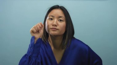 Mavi tişörtlü genç Çinli bir kadın izole edilmiş mavi bir arka plana karşı kapıyı çalıyor. Merakını ve ilgisini gösteriyor..