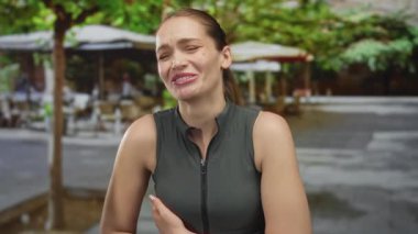 Kafkasyalı genç bir kadın güneşli açık hava restoranının terasında elleri kapalı güler; kaygısız neşe kahkahaları keyif verir.