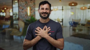 Otel lobisinde elleri göğsünde gülümseyen sakallı İspanyol bir adam, zarif dekorlu bir ev ortamında sıcaklığı ve dostluğu iletiyor..