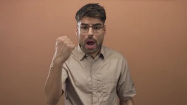 Stüdyoda şeftali duvarına karşı sıkılmış yumruğu ve büzüşmüş dudakları olan İspanyol bir adam..