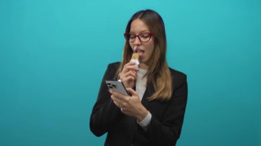 Akıllı telefonu kontrol ederken granola yiyen ve tek eliyle atölyenin tepe zemininde kaydıran kırmızı gözlüklü ve spor ceketli bir kadın..