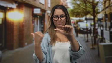 Gözlüklü ve sarı tırnaklı bir kadın, kot gömlek ve beyaz kolsuz bluz giyerken sokakta kendini gösteren başparmaklar; kendine güven cesareti.