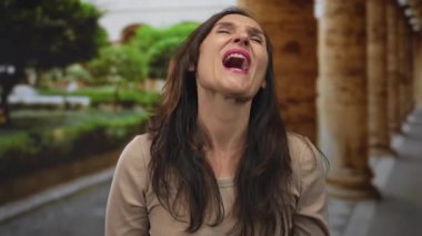 Arka planda sütunları olan yaşlı bir kasaba caddesinde neşeyle gülen genç İspanyol kadın..