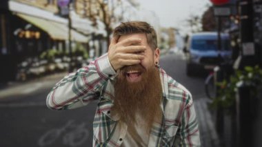 Kafeler ve arabalarla dolu hareketli bir şehir caddesinde gözlerini kapayan genç sakallı adam..