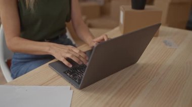 Dizüstü bilgisayarla çalışan bir kadın yeni bir apartman dairesinde kutuları taşırken masada bir bitki, çağdaş bir iç mekanda yeni bir başlangıç olduğunu gösteriyor..