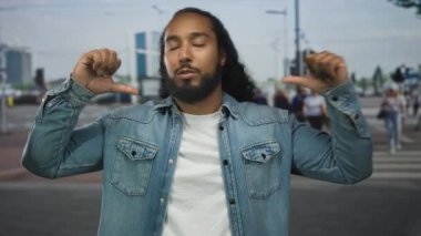 Sakallı ve kot ceketli bir adam, parmakları kenar mahalle yaya geçidinde kendini gösteren bulanık yayalar ve binalar; güven gururu.