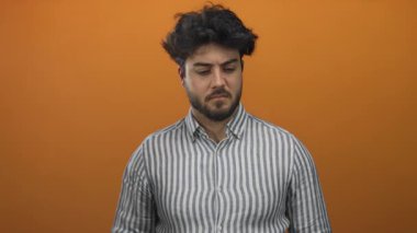 Burnu turuncu bir arka plan karşısında kötü kokudan korunan sakallı genç İspanyol bir adam. İğrenç bir yüz ifadesi var ve çizgili bir gömlek giyiyor..