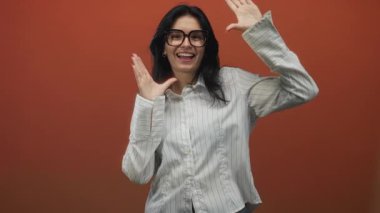Turuncu stüdyoda gözlük takan kadın, elleri olan ve geniş bir gülümseme takınıyor; neşe yaratıcılığı.