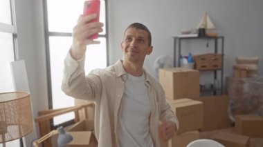 Parlak oturma odasında gülümseyen bir adam yeni daireye taşındığını gösteren karton kutularla çevrili..