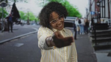 Çizgili gömlek içinde gülümseyen kadın hareketli sokakta el sıkışmak için elini uzatır; sıcak karşılama dostluğu yoldaşlık.