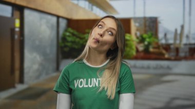 Yeşil tişörtlü genç bir kadın arka planda bitki ve binaların olduğu bir sokakta gülümsüyor..