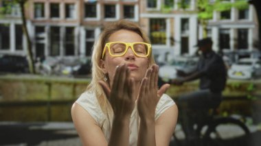 Sarı güneş gözlüğü takan bir kadın iki eliyle öpücükler savuruyor..