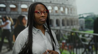 Kolezyumun dışında duran bir kadın, Roma 'da gözlük takıyor ve uzun saçlı çizgili bir gömlek giyiyor, arka planda insanlarla çevrili, samimi bir anı yakalıyor..