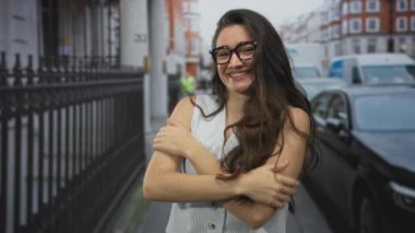 Gözlüklü ve kolsuz tişörtlü genç İspanyol kadın tarihi binaların yakınındaki bir şehir sokağında çıplak kollarına sarılıyor..