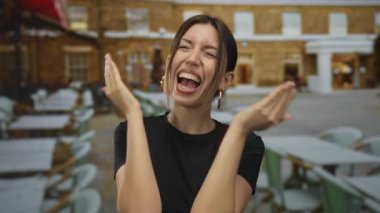 Genç İspanyol kadın ellerini kaldırarak gülüyor ve teras inşaatına kapalı bakıyor..