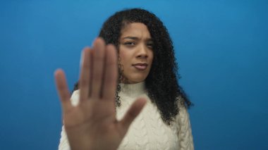 Kadın stüdyoda el ele tutuşuyor. Avuç içleri kameraya dönük ve ciddi bir ifadeyle dur hareketi yapıyor..