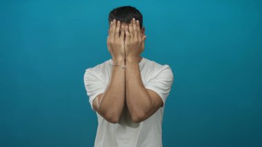 Sıradan beyaz tişörtlü bir adam iki eliyle şakaklara bastırıyor ve parlak mavi bir stüdyo ortamında nazikçe gülümsüyor;.