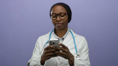 Akıllı telefondan mesaj atan kadın doktor. Mor duvar arkasında steteskop ve gözlüklerle izole edilmiş. Tıp alanında iletişim ve teknoloji olduğunu gösteriyor..