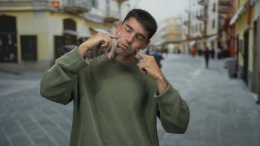 Genç İspanyol adam şehir merkezinde dar bir kaldırım taşı caddesinde parmaklarıyla yanaklarına bastırıyor; yorgunluk.