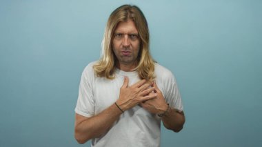 Açık mavi stüdyoda uzun saçlı, terleyen, yüzünü buruşturan ve göğsünü sıkan sarışın bir adam..