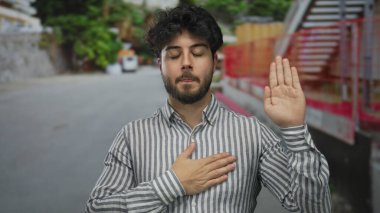 Genç bir İspanyol, güneşli bir günde göğsü açık havada yemin ediyor. Arka planda bulanık ağaçlar ve binalar olan çizgili bir gömlek giyiyor..