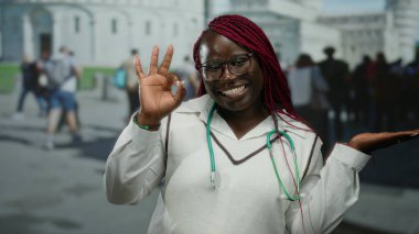 Steteskop hareketleriyle Afro-Amerikalı kadın tamam ve kalabalık bir şehir caddesinde elini gösteriyor..