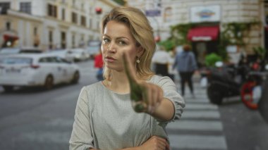 Sarışın kadın şehir merkezinde yoğun bir caddede sert bir ifadeyle kamerayı işaret ediyor. Cesur bir meydan okuma..